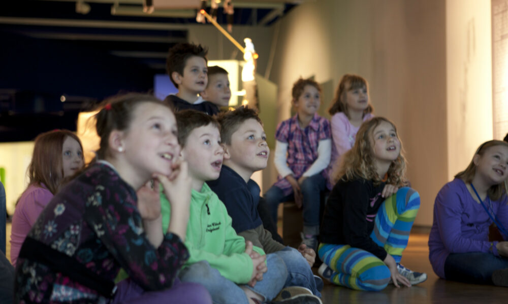 Kinder in der Ausstellung im Museum für Kommunikation schauen gespannt auf einen Punkt, der nicht im Bild liegt.