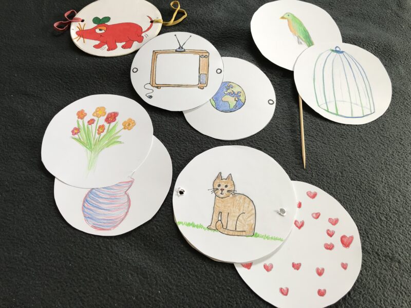 Mit Symbolen und Tieren bemalte Papierkreise, Gummis und ein Holzspieß, die zum erstellen von Wunderscheiben bereit liegen.