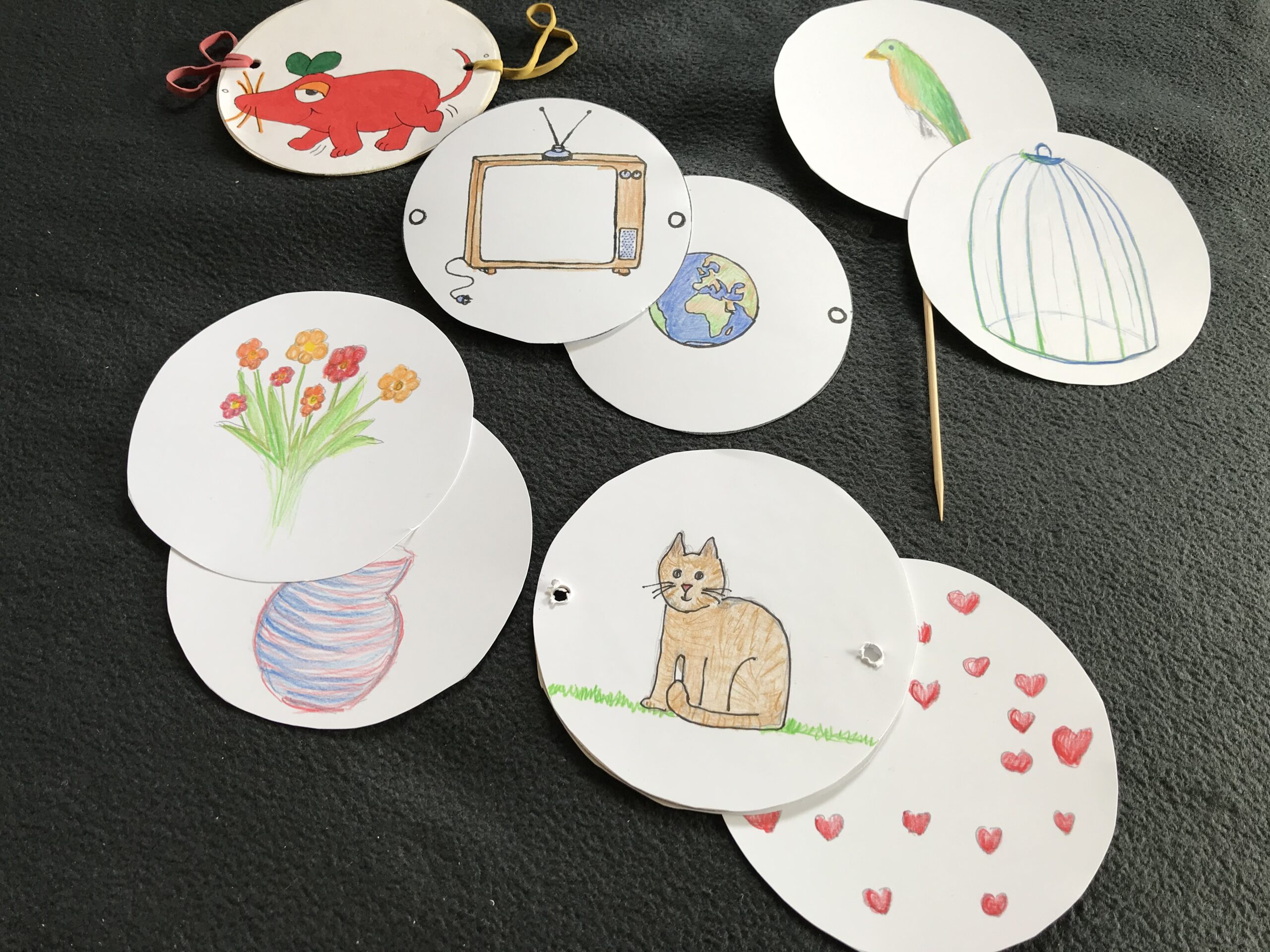 Mit Symbolen und Tieren bemalte Papierkreise, Gummis und ein Holzspieß, die zum erstellen von Wunderscheiben bereit liegen.