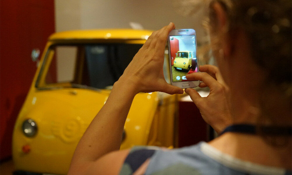 Eine Frau fotografiert die gelbe Post Isetta im Museum für Kommunikation Nürnberg