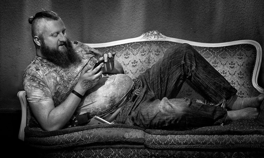 Ausstellung Kontaktabzüge: Mann mit Bart auf Sofa, Smartphone in der Hand